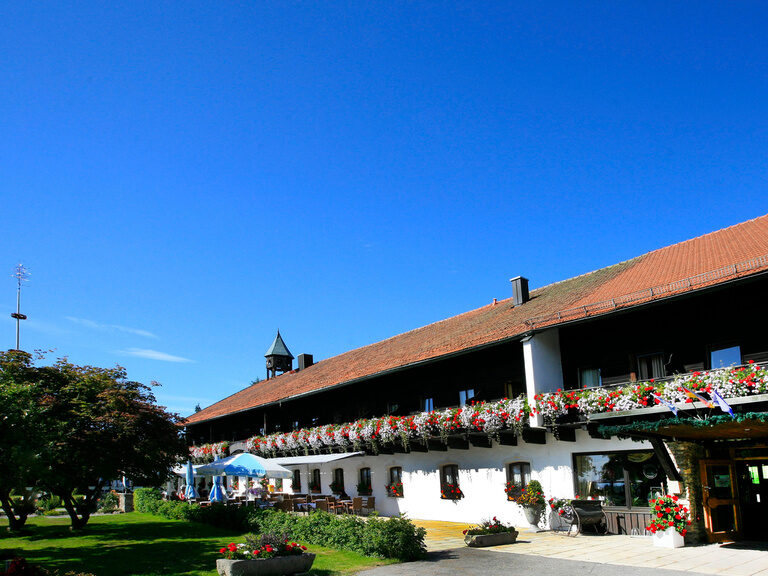 Der Eingang und das Gebäude des Hotel Gut Schmelmerhof in Sankt Englmar an einem schönen Sommertag.